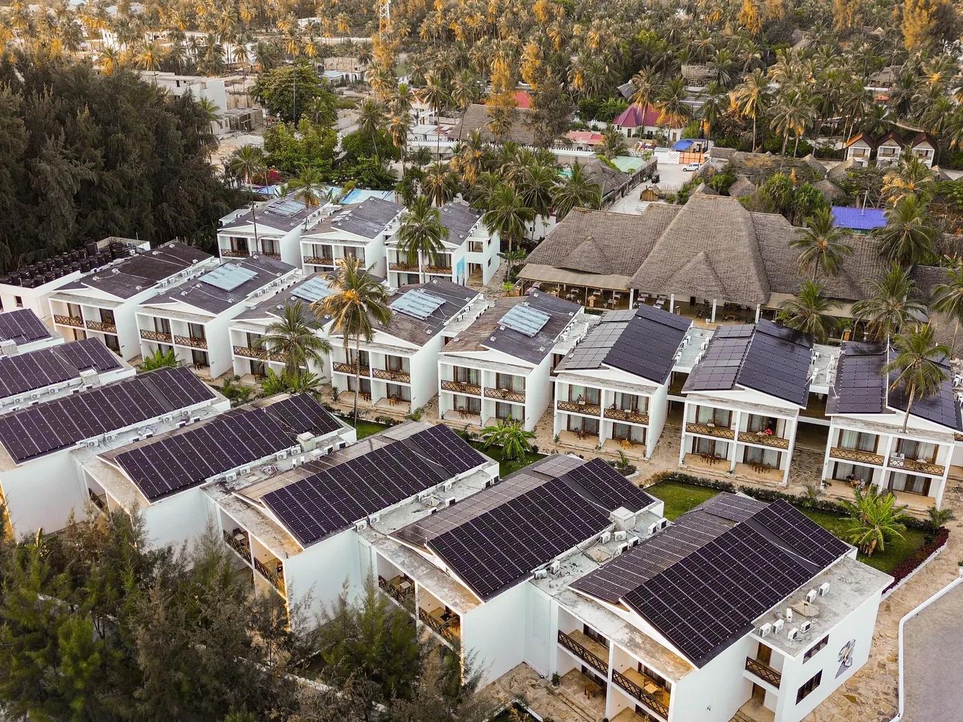 Resort villas with solar roofs among palms at golden hour, seen from the drone