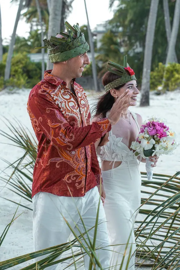 Groom gently touching the bride’s cheek on the beach, bouquet in her hand