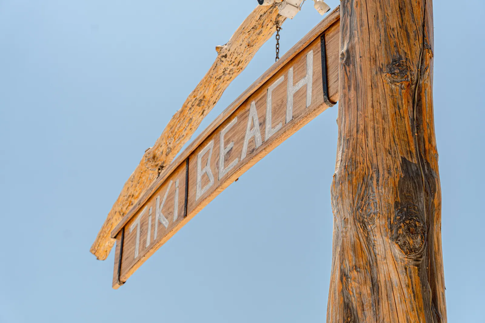 Wooden Tiki Beach sign hanging from a post against a clear sky